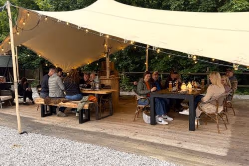 Gruppe von Gästen beim gemeinsamen Essen unter dem überdachten Zeltdach auf der Terrasse des Iris Valley Lodge in Herzberg am Harz, ideal für Gruppen und Vereine im Harz