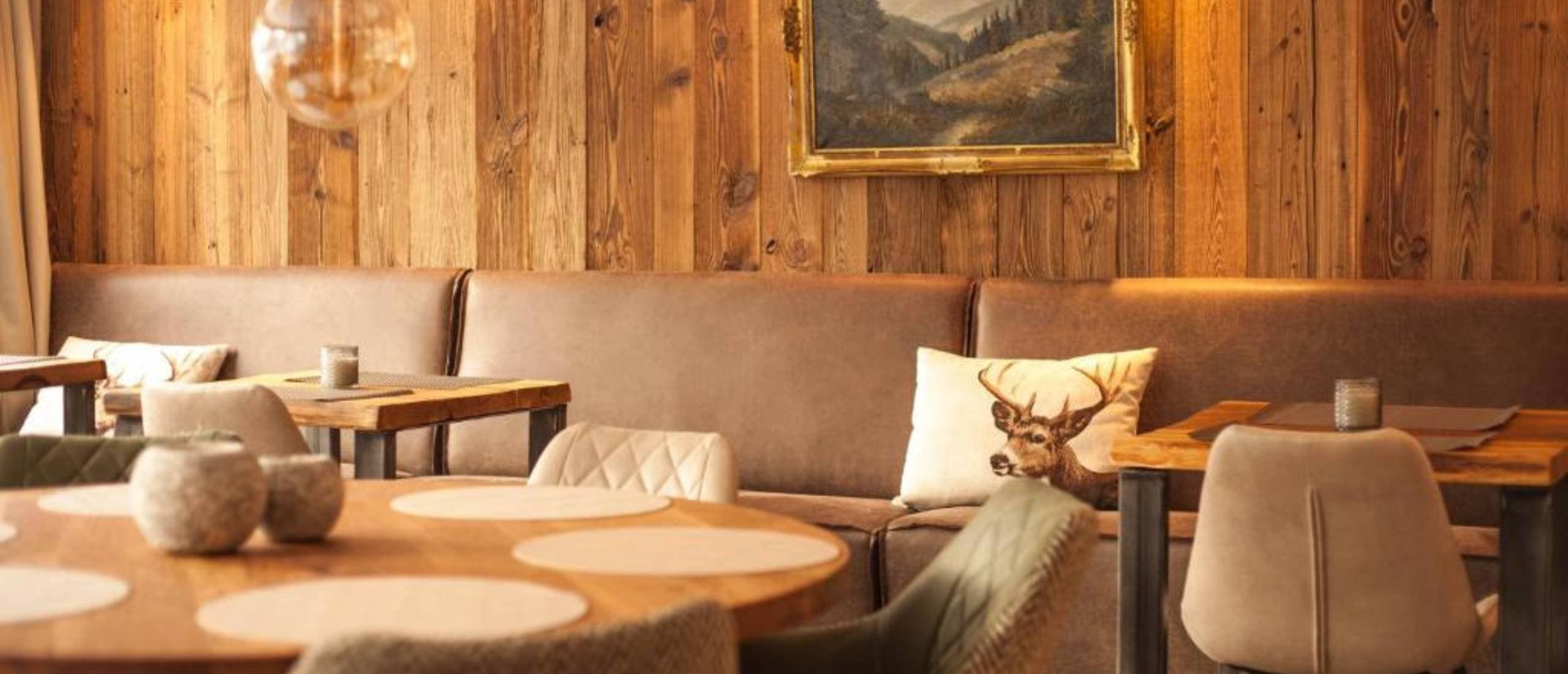 Gemütlicher Restaurantbereich im Iris Valley Lodge mit Holzwänden, Lederbänken und Hirschmotiv-Kissen